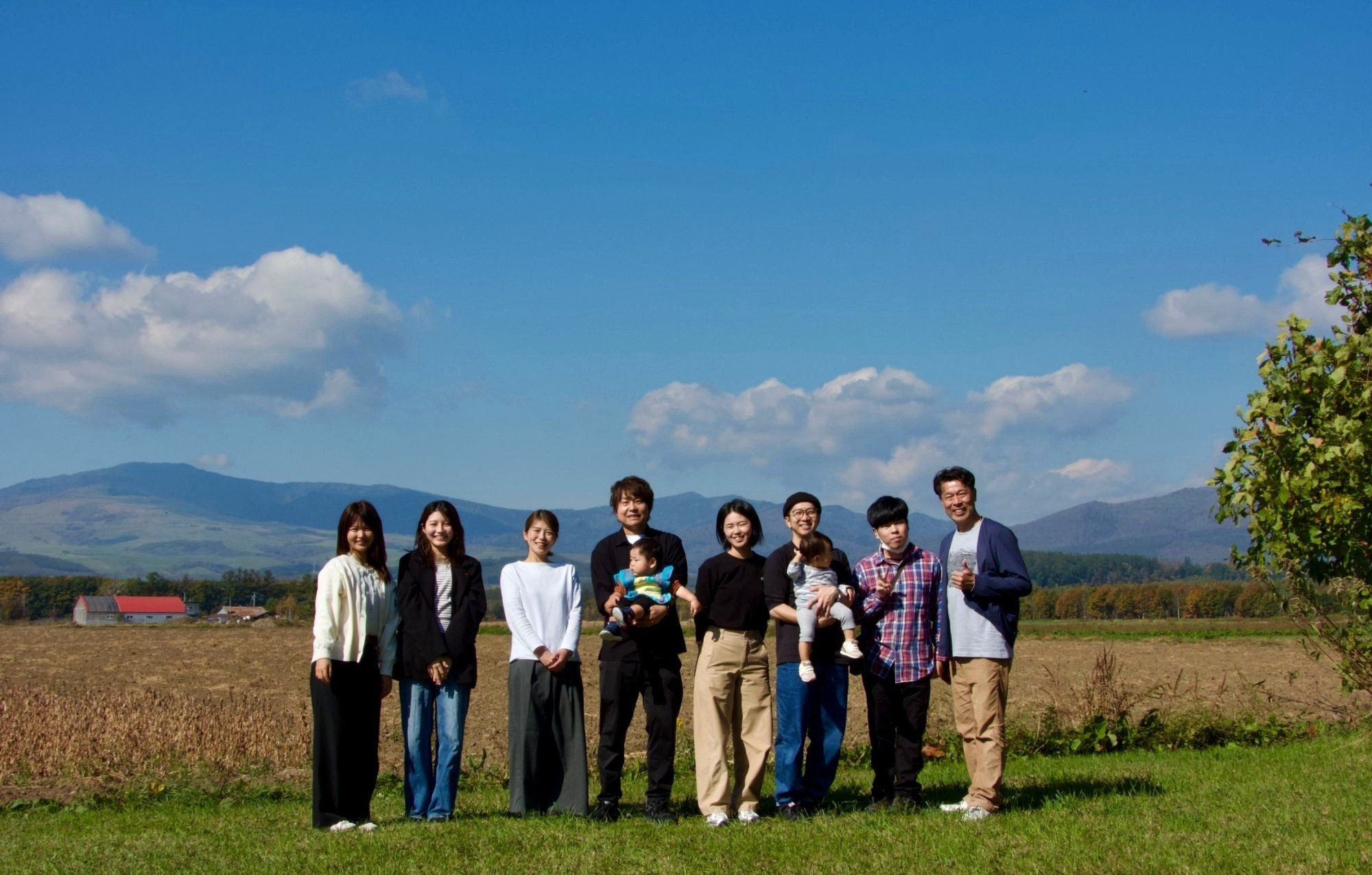 Grass Family.のメンバーが、青空と山を背に、野原に並んで立っている集合写真